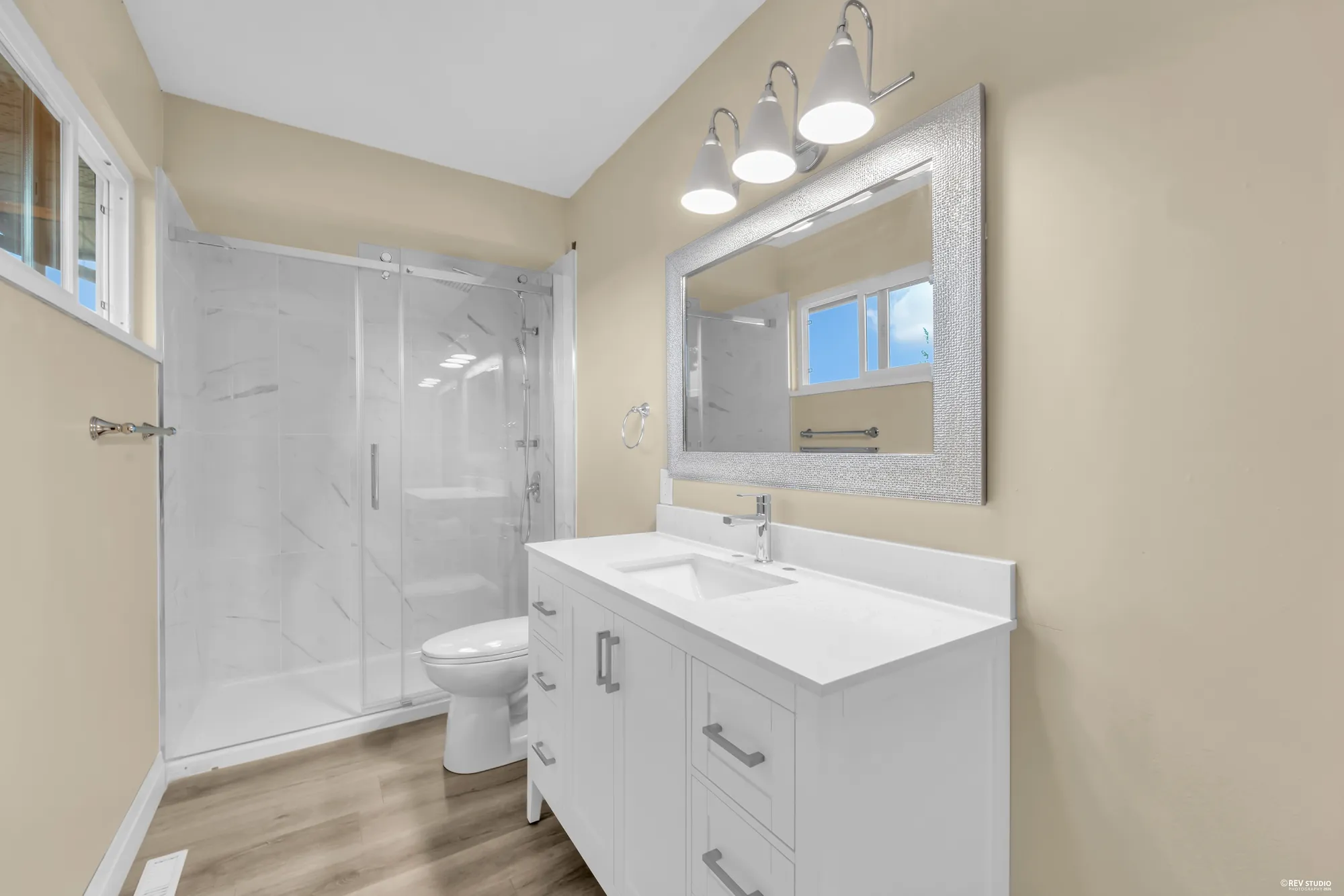 The upstairs bathroom with a glass shower, a white vanity and a window