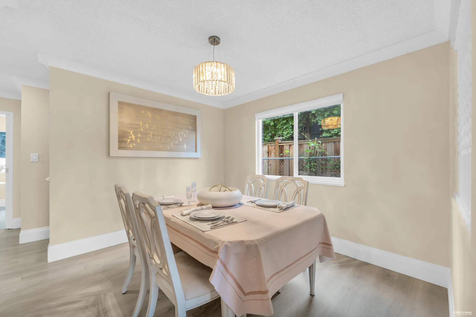 The dining room with a dressed table under a crystal pendant and a window to the side