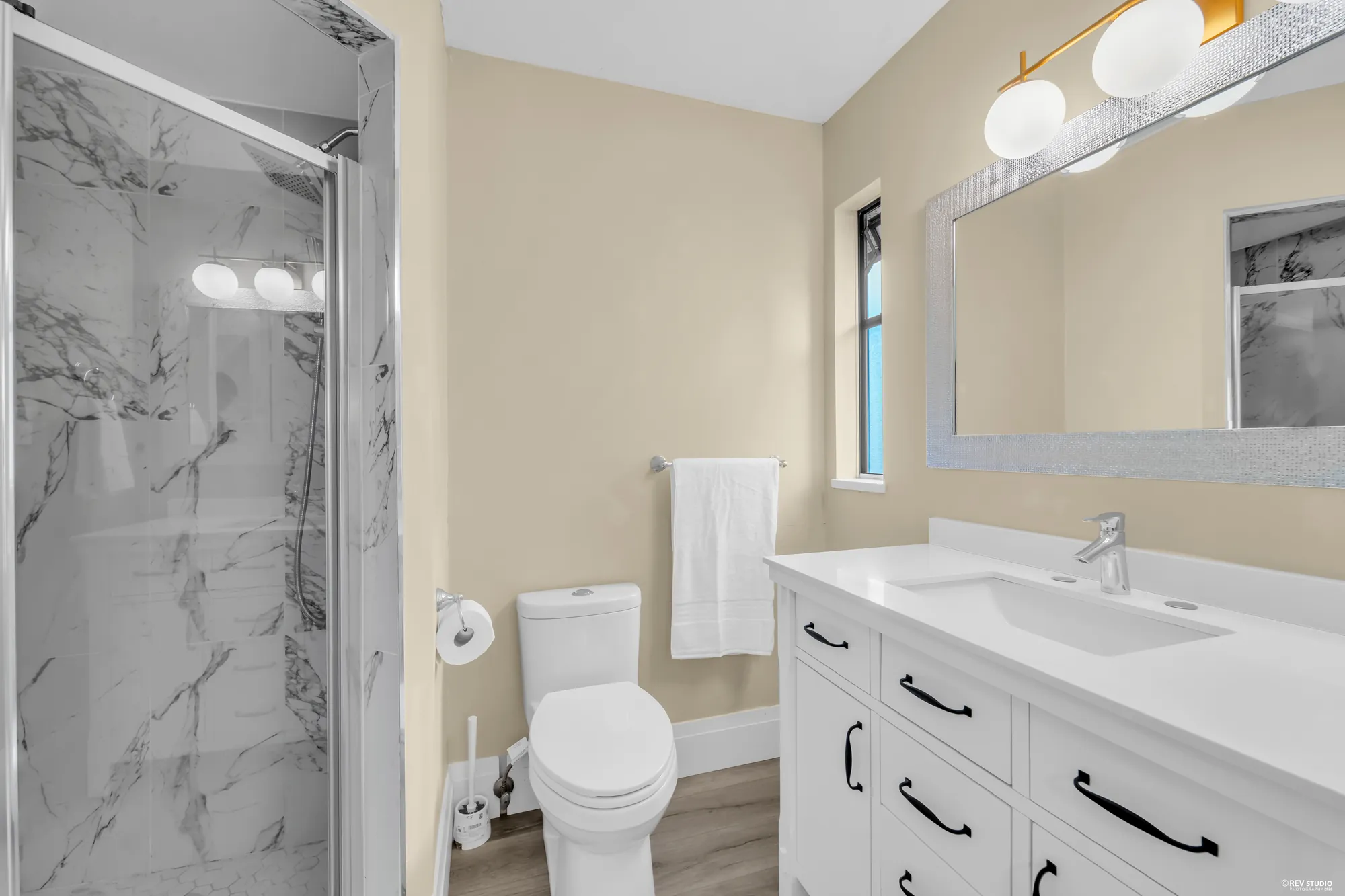The primary bathroom with a marble-look shower, a white vanity and a mirror