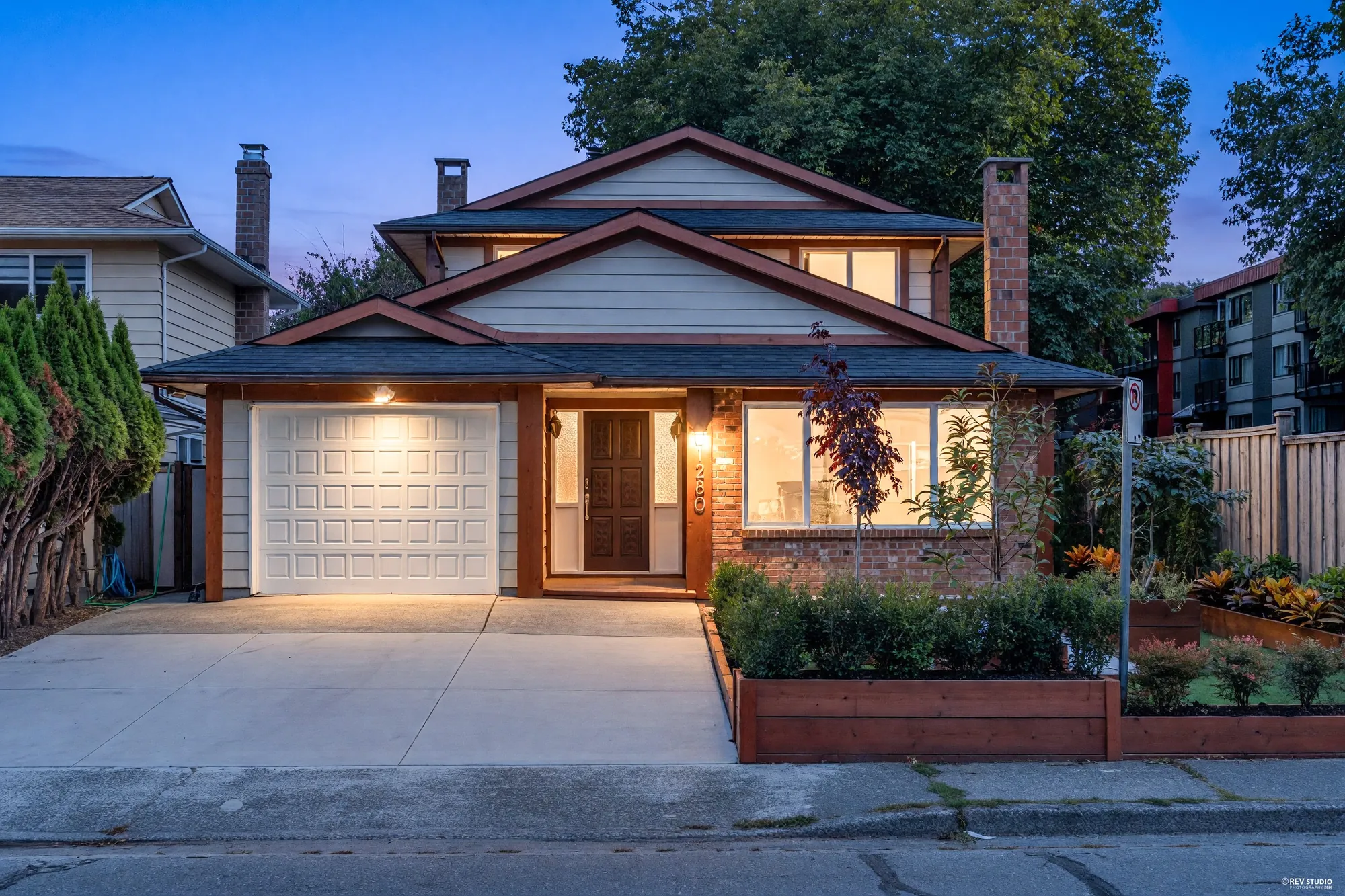 11280 Daniels Road from the street at dusk: brick and cedar trim, the porch light on, raised planters along the drive