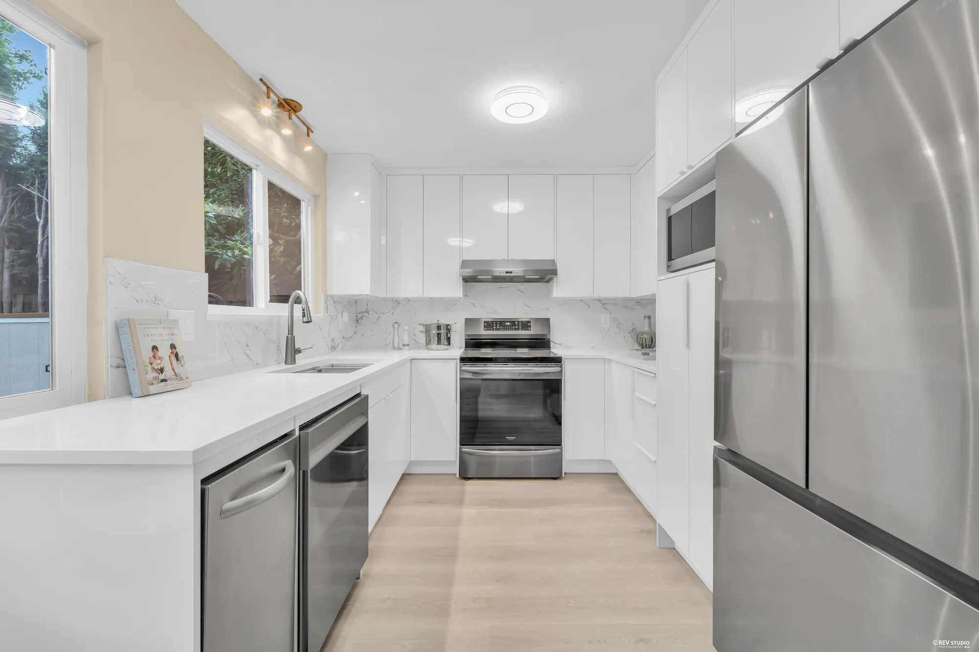 The kitchen: white cabinets, a marbled quartz counter, a stainless range, hood and fridge, and a window over the sink
