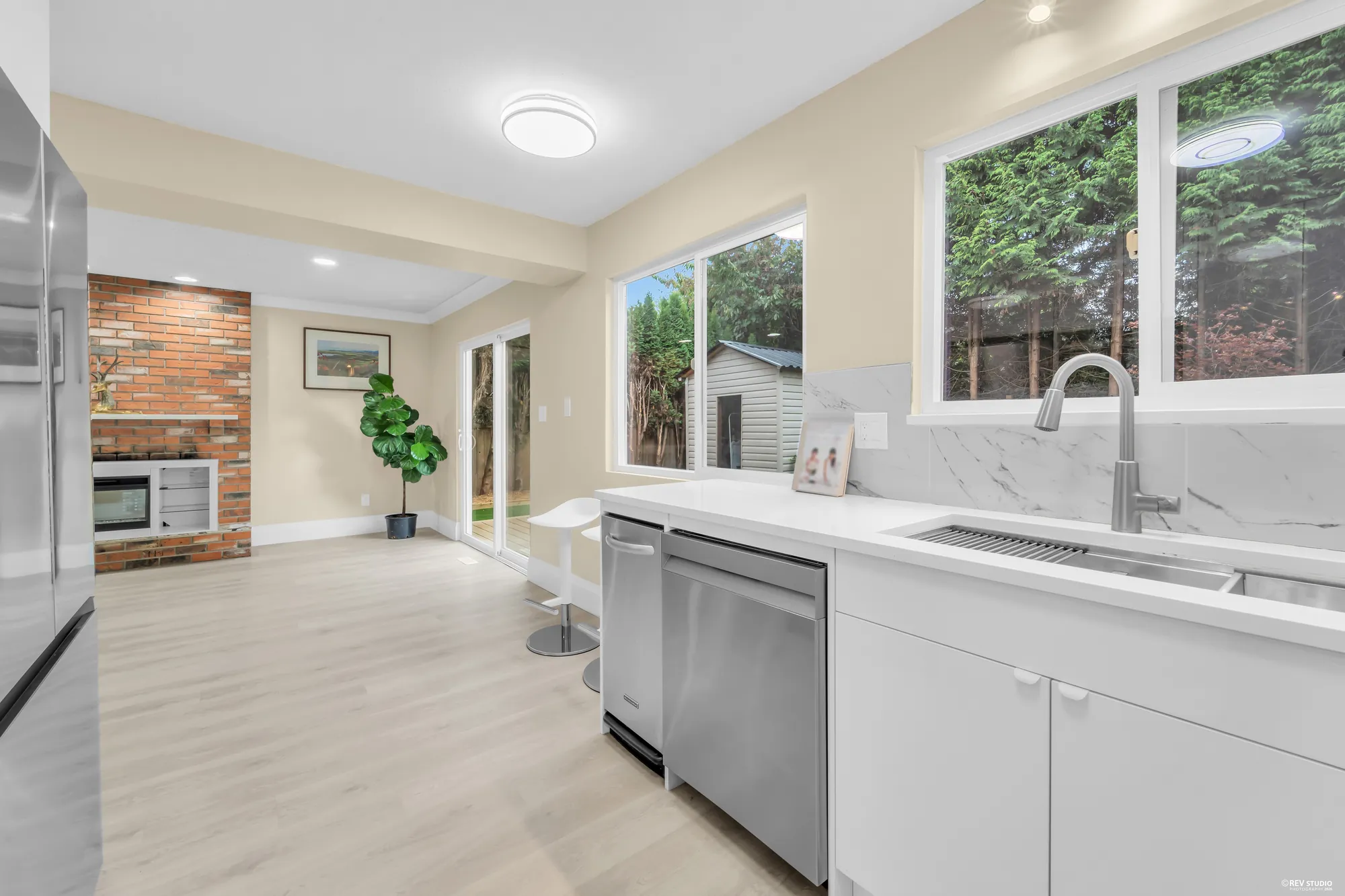 The kitchen counter and sink under the windows, the family room and the door to the deck beyond