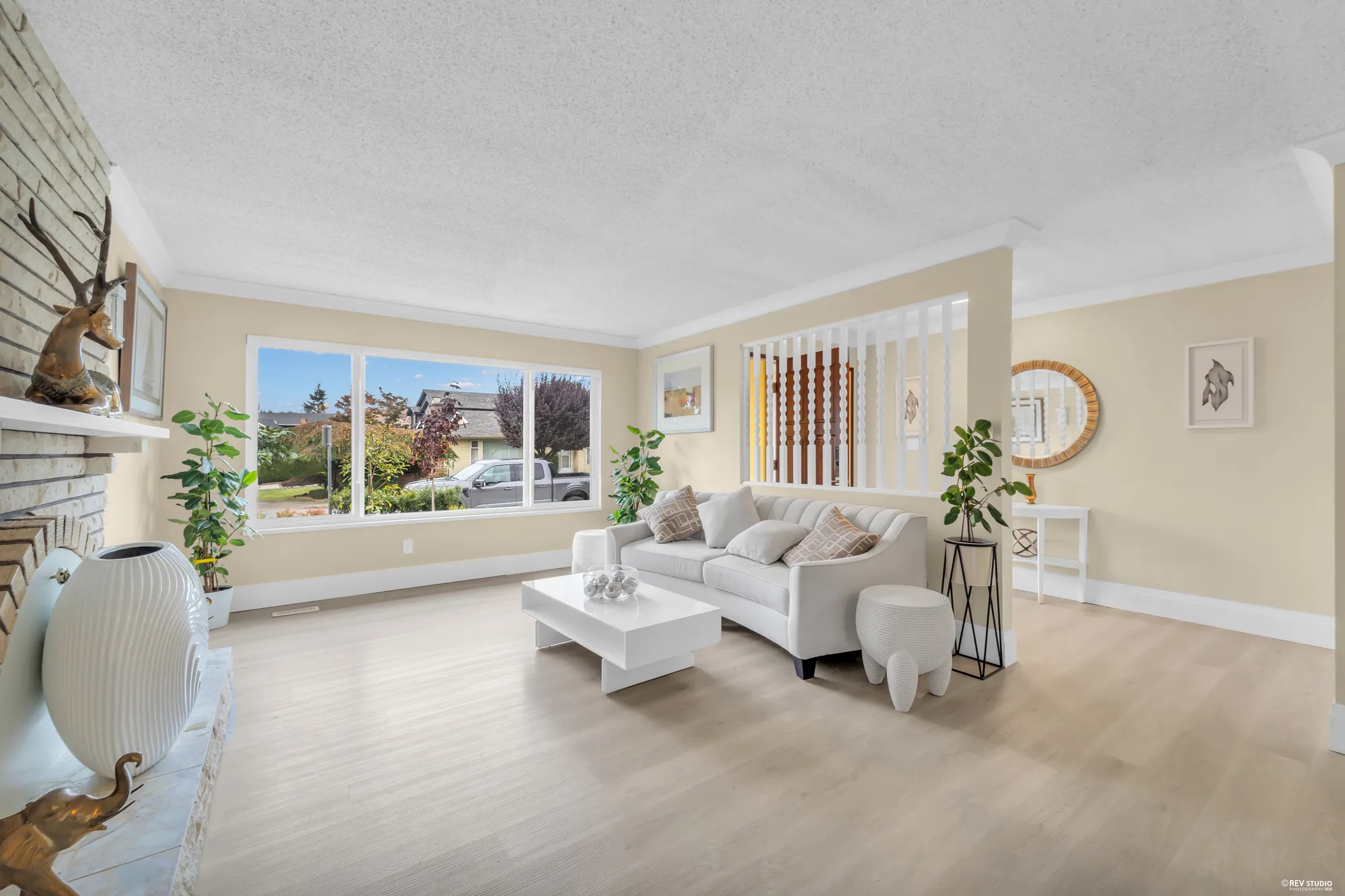 The living room with a pale sofa, the window onto the street and the white-painted brick fireplace