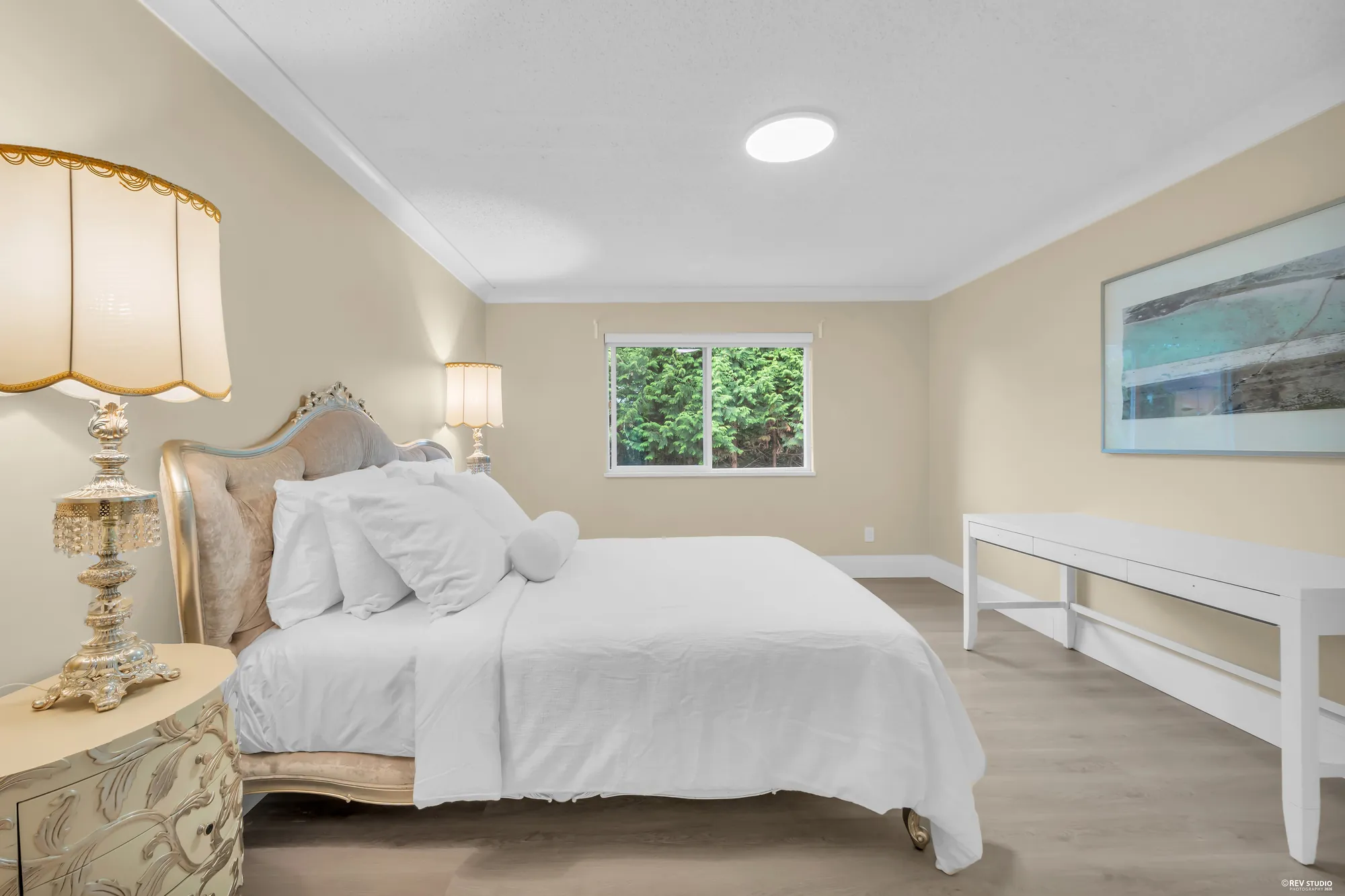 The primary bedroom from beside the bed, a lamp in the foreground and the window beyond