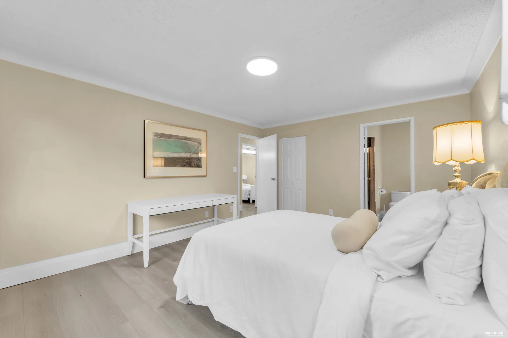 The primary bedroom from the foot of the bed, the doors to the hall and the bathroom beyond