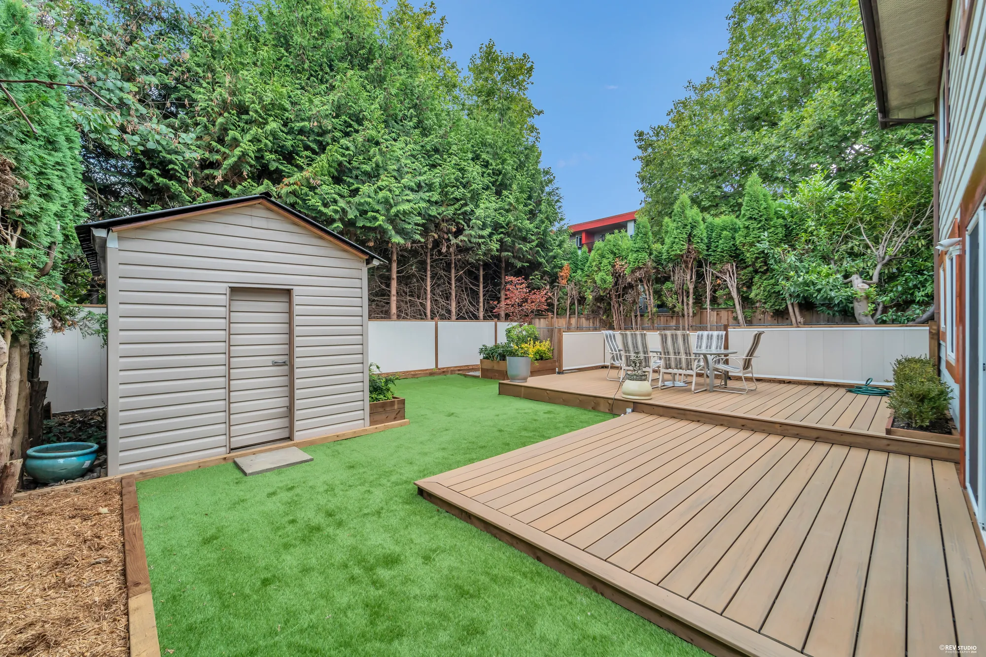 The garden shed at the end of the deck, turf in front of it and the fence behind